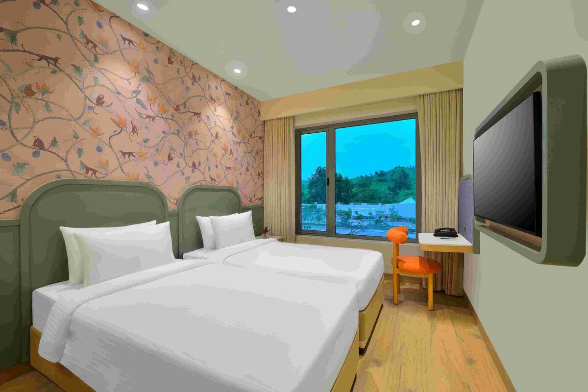 Habitación de hotel con dos camas, televisión, escritorio con silla y ventana con vista a zonas verdes.