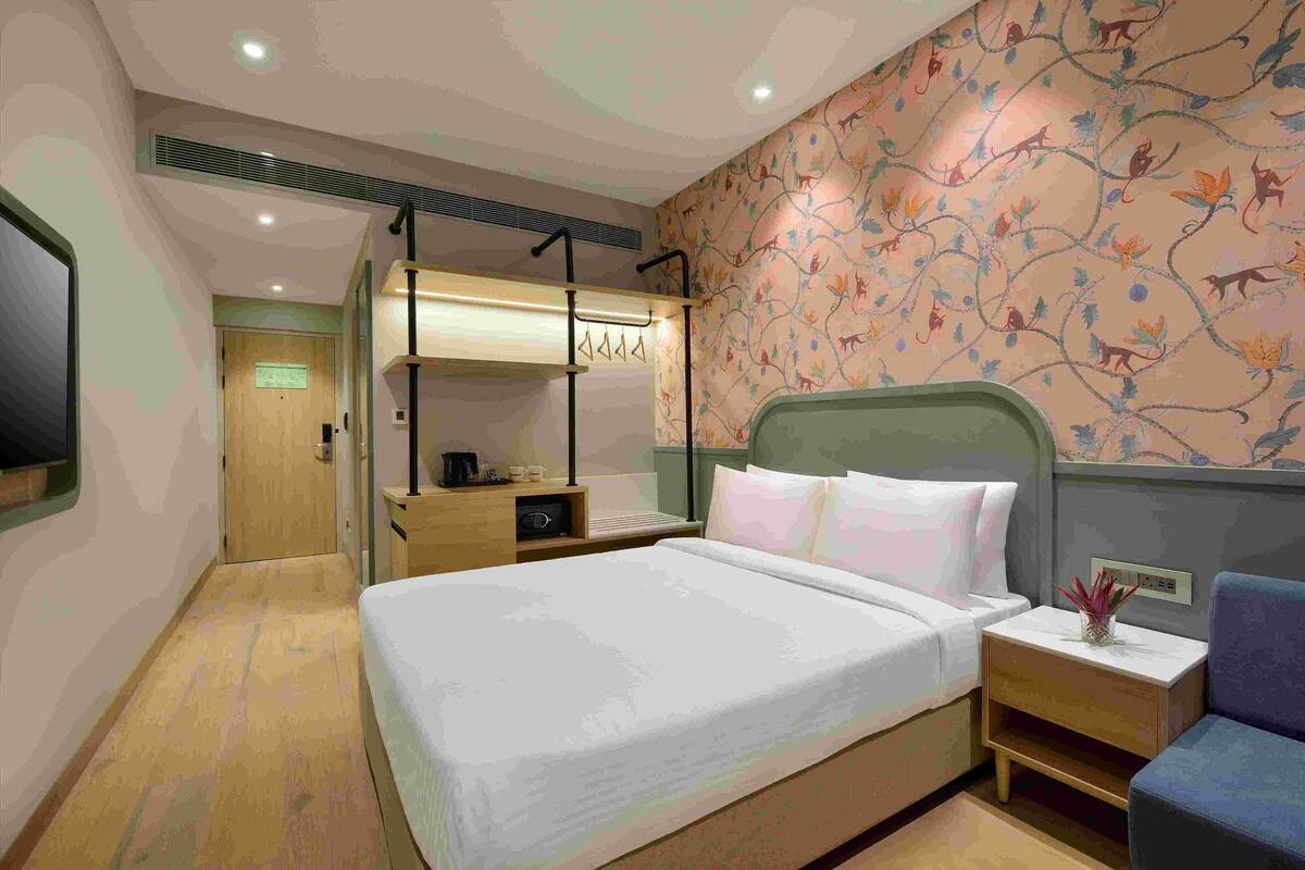 Una habitación de hotel con cama, mesita de noche y televisión montada en la pared.