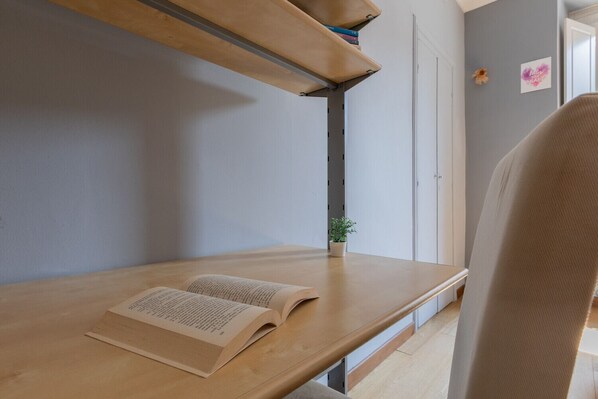 A room with a wooden desk, an open book, a small potted plant, and a chair.