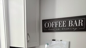 A kitchen with a coffee bar sign, a coffee maker, and a trash bin. - Driftwood Den - Walk to Folly Field Beach from Spacious 3BR/2.5BA Condo (Hilton Head Island)