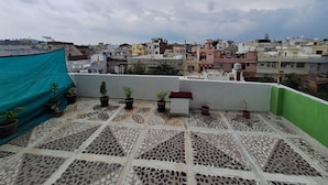 A rooftop terrace with a patterned floor, potted plants, and a view of a densely built cityscape. - Tara Home Stay (Udaipur)