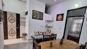A dining area with a round wooden table and chairs, a ceiling fan, and artwork on the walls. - Tara Home Stay (Udaipur)