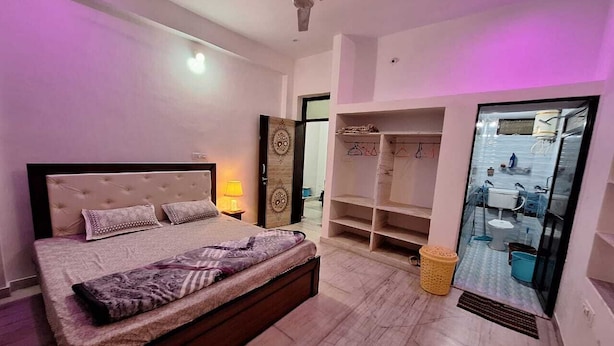 A bedroom with a bed, a wardrobe, a mirror, and a bathroom visible through a glass door. - Tara Home Stay (Udaipur)