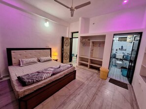 A bedroom with a bed, a wardrobe, a mirror, and a bathroom visible through a glass door. - Tara Home Stay (Udaipur)