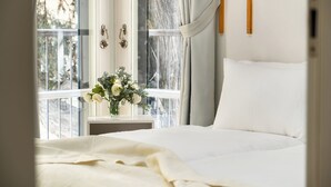 Ein Schlafzimmer mit einem Bett, einem Fenster mit Vorhängen, einer Vase mit Blumen und einer Holzvertäfelung.