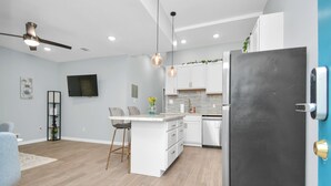 Una cocina moderna con armarios blancos, un refrigerador negro y una zona de comedor con un taburete de bar.