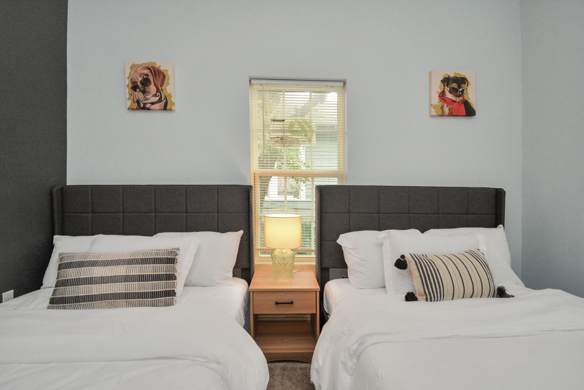 A hotel room with two beds, a nightstand with a lamp, and artwork on the walls.