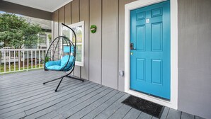 Un porche con una puerta azul, una silla colgante y un pequeño adorno circular.
