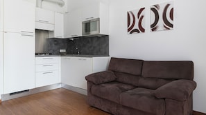 A modern kitchen with white cabinets, a built-in oven, and a grey countertop. There is a brown sofa in the foreground and abstract art on the wall. - Lulli 13 A (Milan)