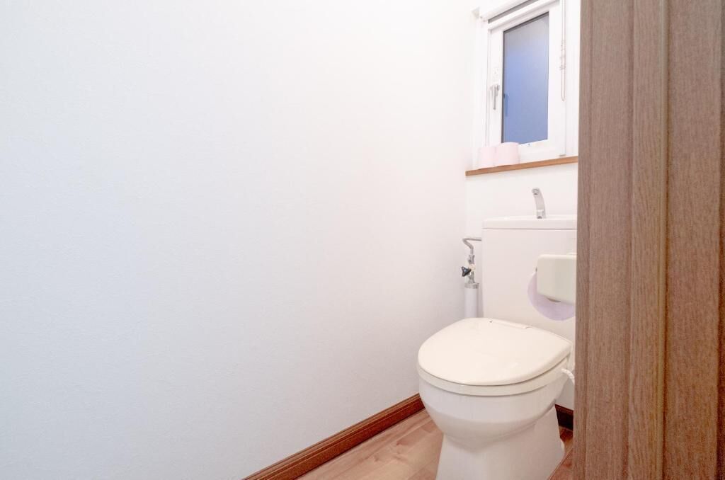 A small, clean bathroom with a toilet, a sink, and a window above the sink.
