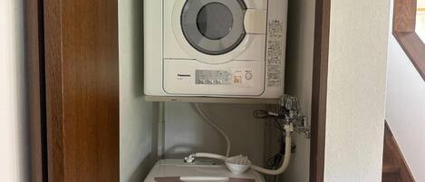 A compact, wall-mounted washing machine with a control panel and a hose connection.