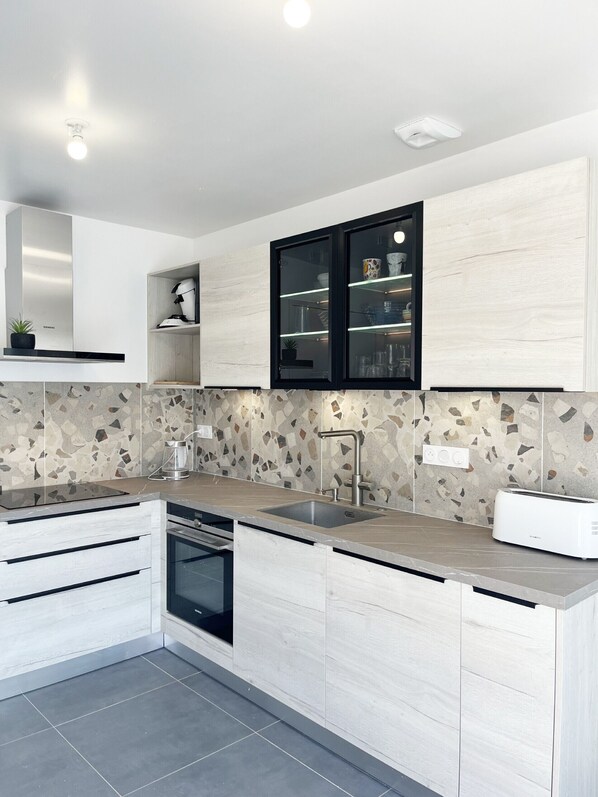 A modern kitchen with white cabinetry, a built-in oven, a stainless steel sink, and a countertop with a mosaic backsplash.
