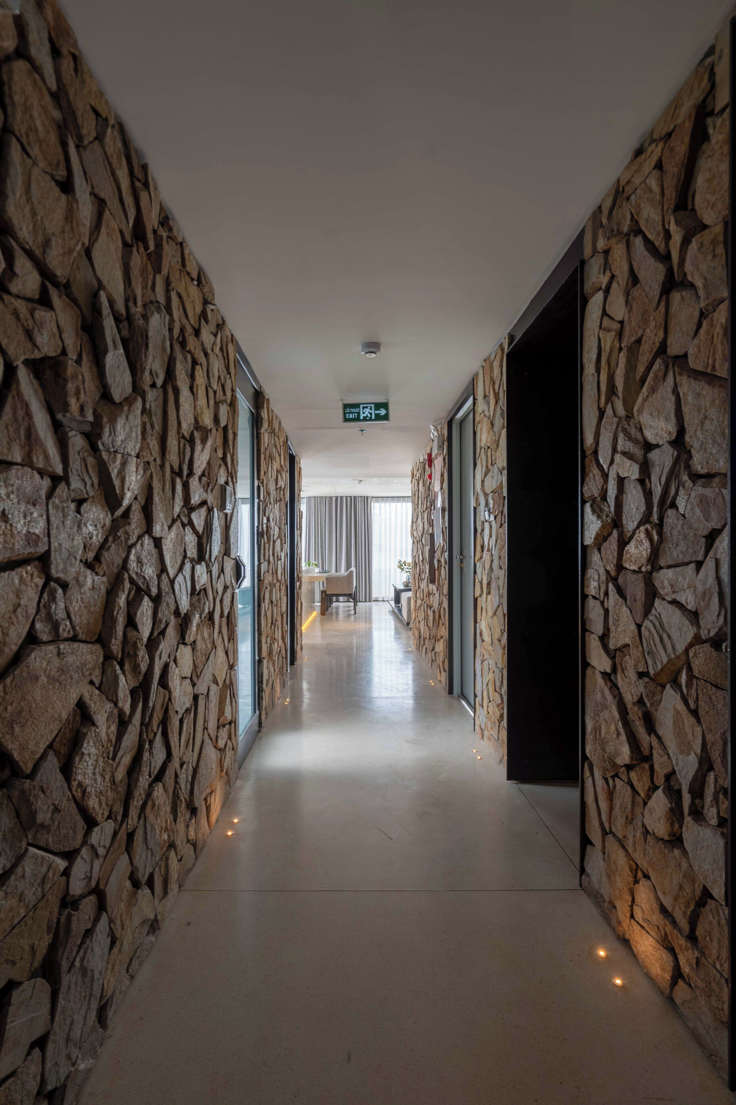 Un pasillo con paredes de piedra y un camino despejado hacia una habitación con cama y ventana.