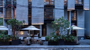 Zona exterior con mesas y sillas, rodeada de plantas en macetas y sombrillas.