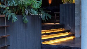Un interior moderno con una escalera que sube a un nivel superior, rodeado de grandes macetas con follaje tropical.