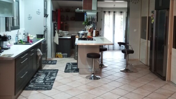 A modern kitchen with a central island, bar stools, and a refrigerator.