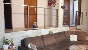 A cozy living room with a brown sofa, a coffee table, and a small stool. There is a window with a metal railing and a potted plant on a side table.