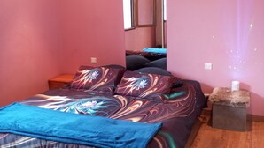 A bedroom with pink walls, a bed with a colorful bedspread, a nightstand, a mirror, and a small wooden stool.