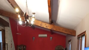 A cozy living room with a red wall, wooden beams, a stone fireplace, a television, and a large barrel.