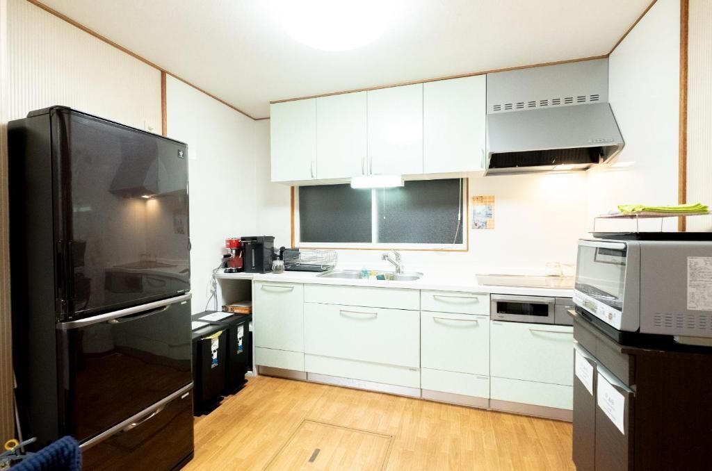 Cocina compacta con refrigerador negro, microondas, pileta y muebles de tonos claros.