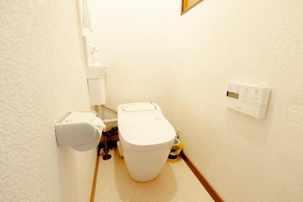 Een kleine, praktische badkamer met toilet, bidet en een bedieningspaneel aan de muur.