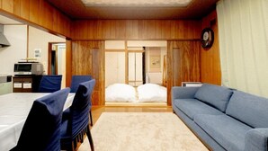 Ein Zimmer mit Holzeinrichtung, einem Bett mit weißer Bettwäsche, einem blauen Sofa und einem Esstisch mit Stühlen.