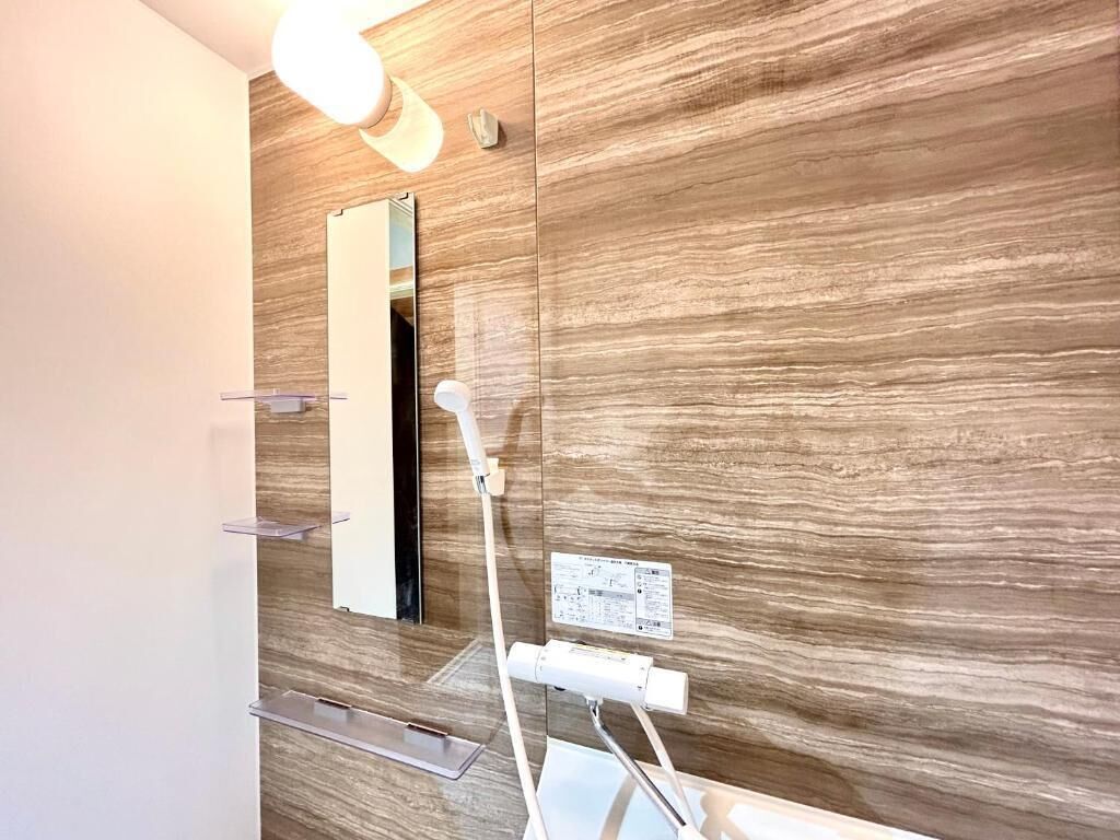 A bathroom with a wooden wall, a mirror, a towel rack, and a shower head.