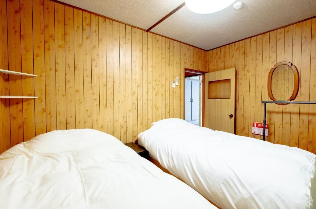 Ein Zimmer mit zwei Betten, Holzwänden, einer Tür und einem kleinen Regal.