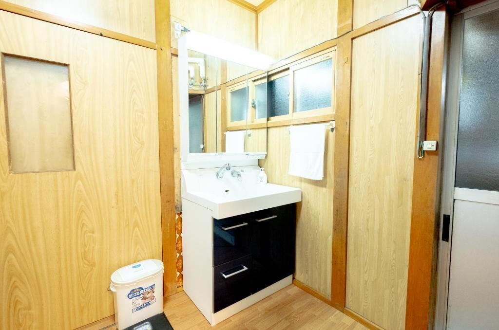 Ein kleines Badezimmer mit Holzwänden, einem weißen Waschbecken, einem Spiegel und einer kleinen Mülltonne.