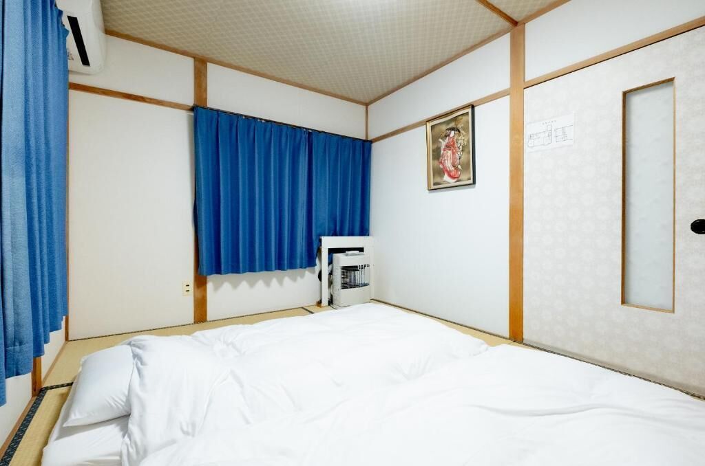 Ein Hotelzimmer mit einem Bett, einem Heizkörper, einem Fenster mit blauen Vorhängen und einer Tür mit einem gerahmten Bild.