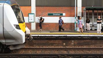 A train station platform with a train approaching, a sign reading 'Streatham,' and a safety warning 'MIND THE GAP.'