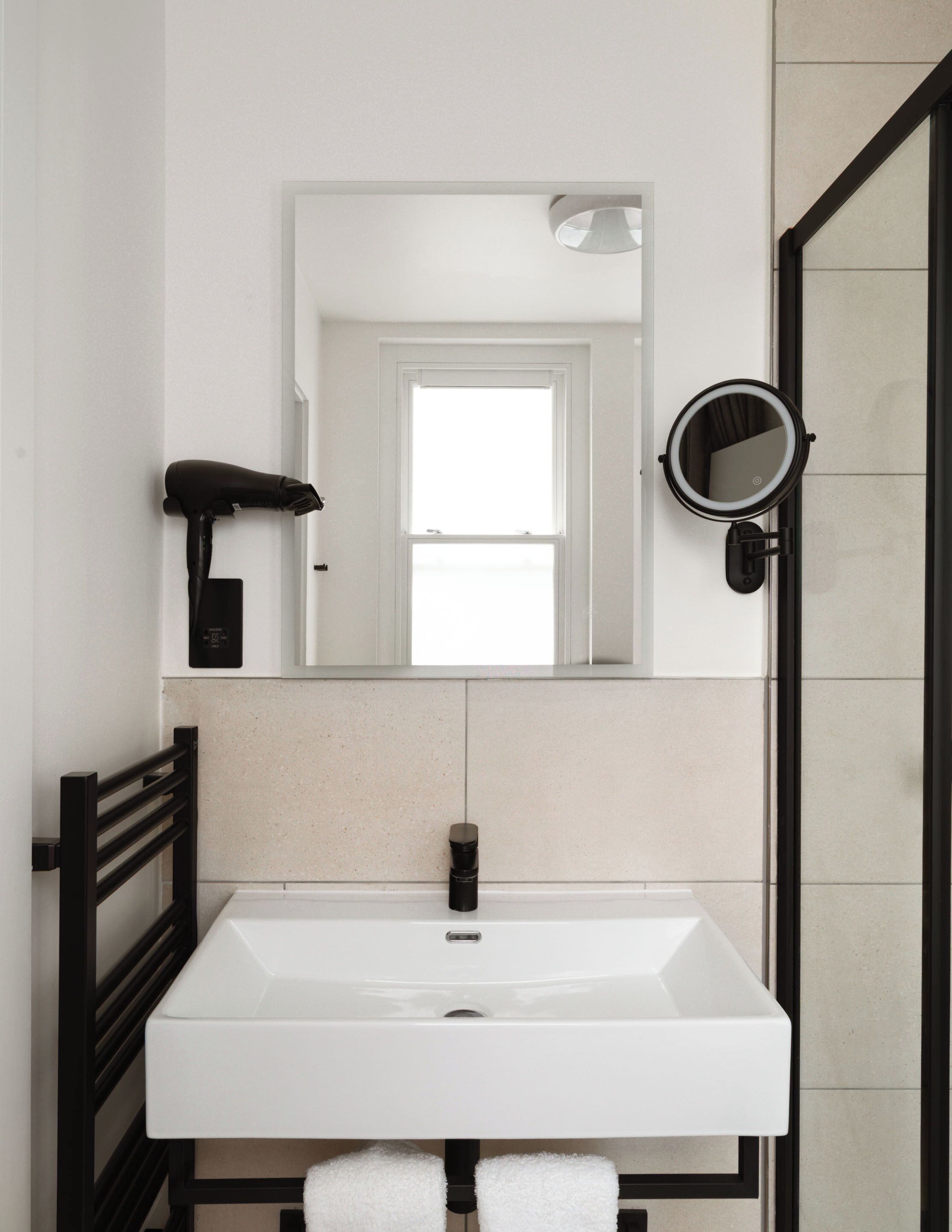 A bathroom with a white sink, a black towel rack, a mirror, and a hairdryer.