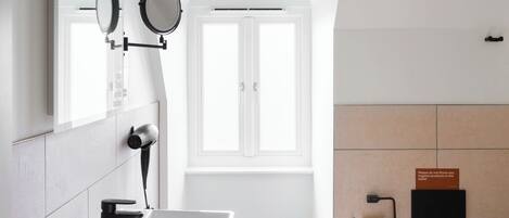A modern bathroom with a white sink, a mirror, a toilet, and a window.