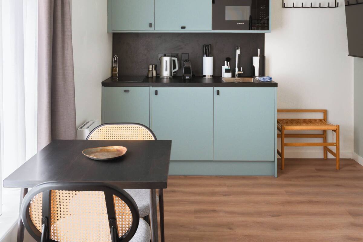 A compact kitchen with light blue cabinets, a dark wooden table, and a wicker chair.