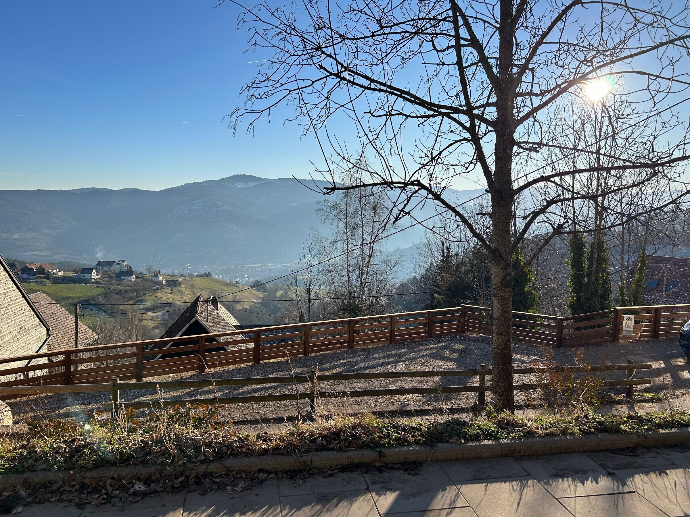Blick von einem Balkon über ein Tal mit Häusern und Bergen in der Ferne.