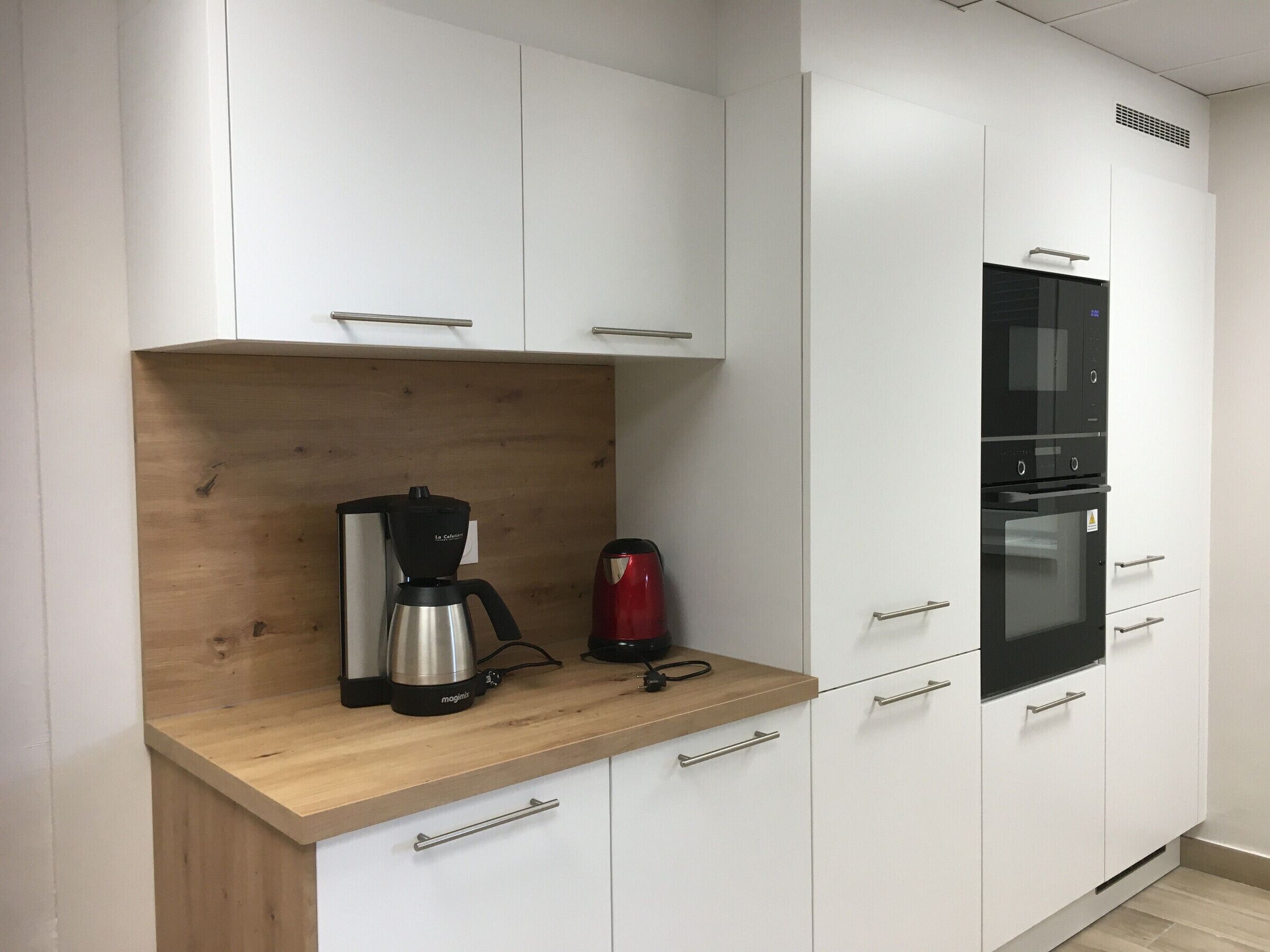 Eine moderne Küche mit weißen Schränken, einer Holz Arbeitsplatte, einer Kaffeemaschine, einem roten Wasserkocher und einem eingebauten Backofen.