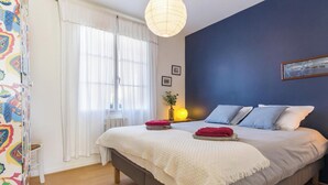 A bedroom with a bed, a bedside table with a lamp, a window with curtains, and a wall with a picture. - Charming South Garden Apartment, Pets Allowed, Parking, Barfleur (Barfleur)