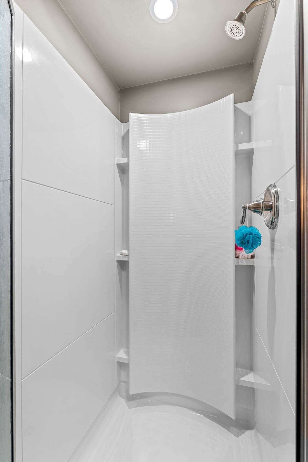A modern shower enclosure with a glass door, a showerhead, and a shelf with toiletries.
