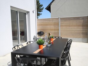 Eine Terrasse im Freien mit einem schwarzen Tisch und Stühlen, einem Holzzaun und einem Grill.