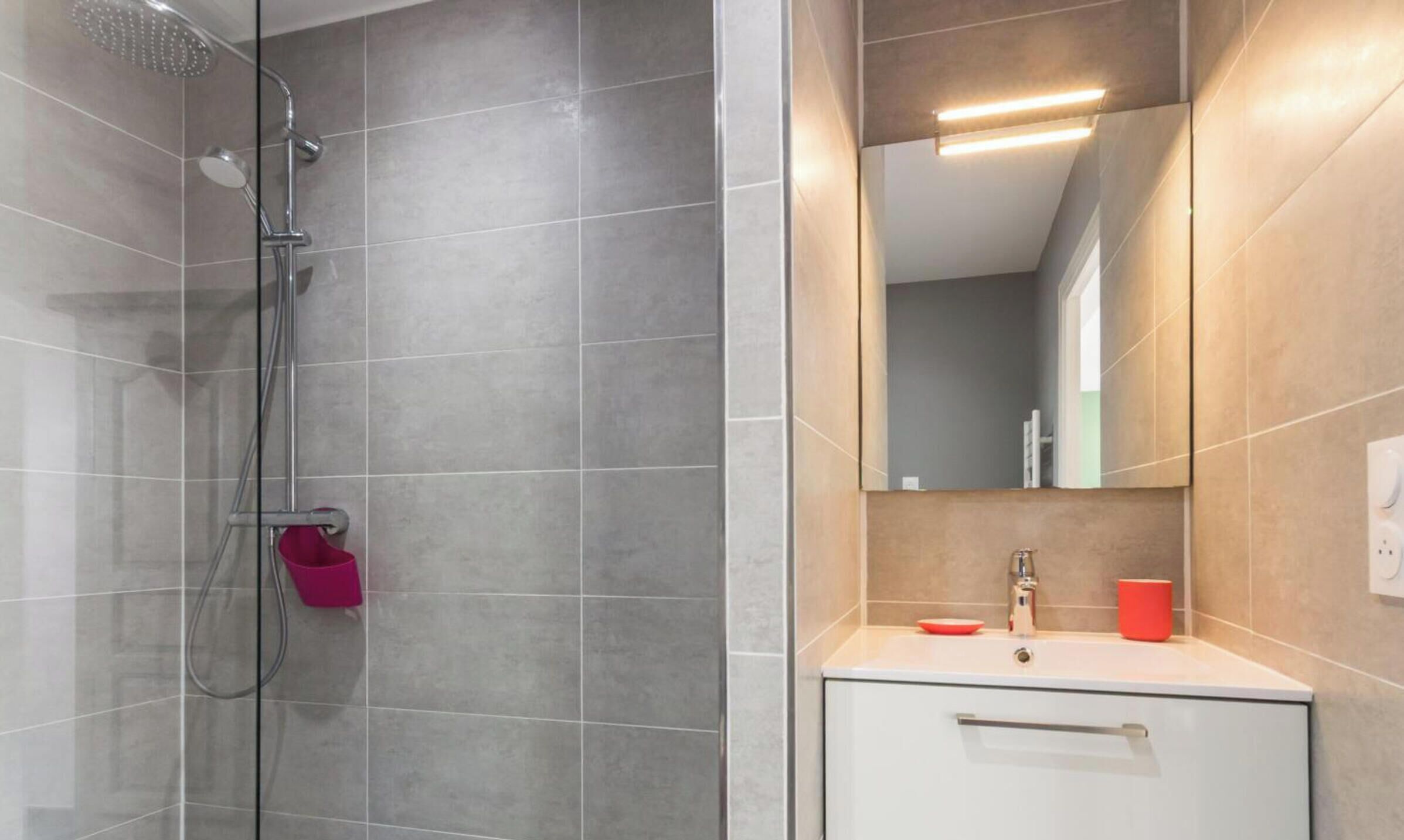 A modern bathroom with a shower, a sink, and a mirror.