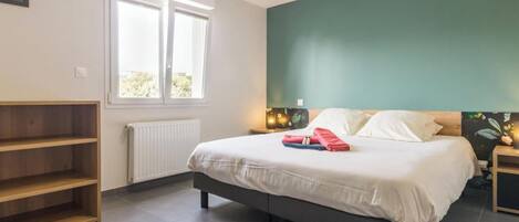 Ein Schlafzimmer mit Bett, Fenster, Heizkörper, Ablagefläche und Wand mit grüner Akzentfarbe.
