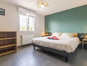 Une chambre à coucher comprenant un lit, une fenêtre, un radiateur, une étagère et un mur avec une touche de couleur verte.