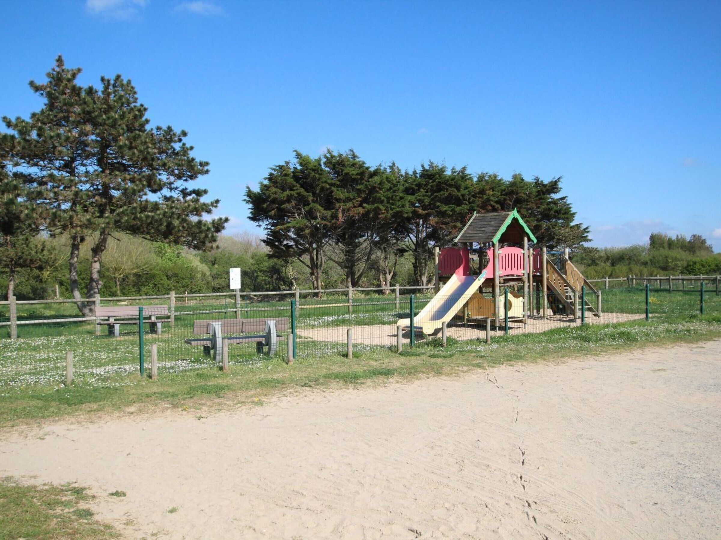 A playground with a slide and climbing structures, surrounded by a fence and benches.