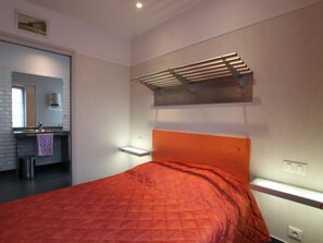 Ein Schlafzimmer mit einem Bett, einer eingebauten Ablage, einem Spiegel und einem Fenster.