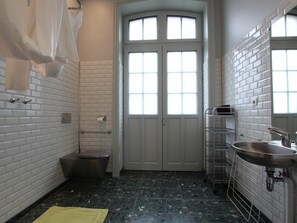 Ein Badezimmer mit weißen Ziegelsteinfliesen, einem schwarzen Marmorboden, einer weißen Tür mit Glasfeldern, einem Waschbecken mit einem Metallregal und einem Handtuch an einem Haken.