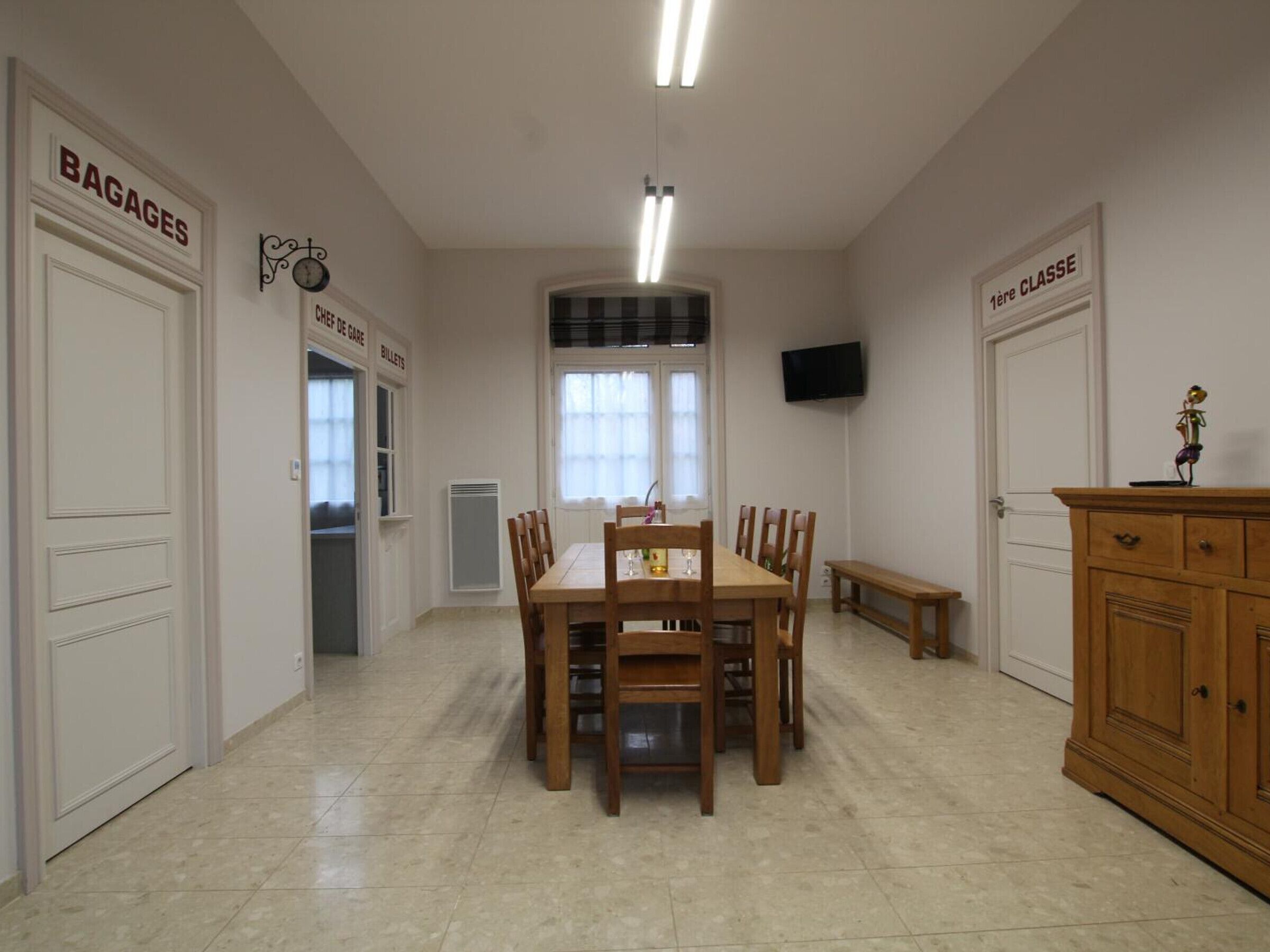 A dining area with a wooden table and chairs, a bench, a cabinet, and a television on the wall.