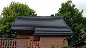 Een houten huis met een donker dak, omringd door weelderig groen gebladerte.