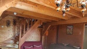 Een houten interieur met een trap, een bank met kussens, een tafel en een muur met een schilderij.