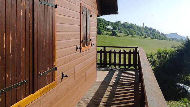 Een houten gebouw met grote ramen en een balkon met uitzicht op een groen landschap.