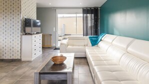 Un salon moderne avec un canapé blanc, une table basse et un téléviseur posé sur un meuble.